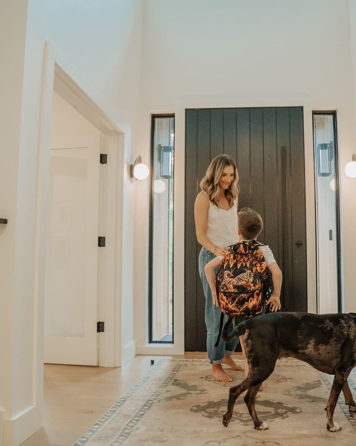 A child with a backpack heading for the front door with a parent and the dog