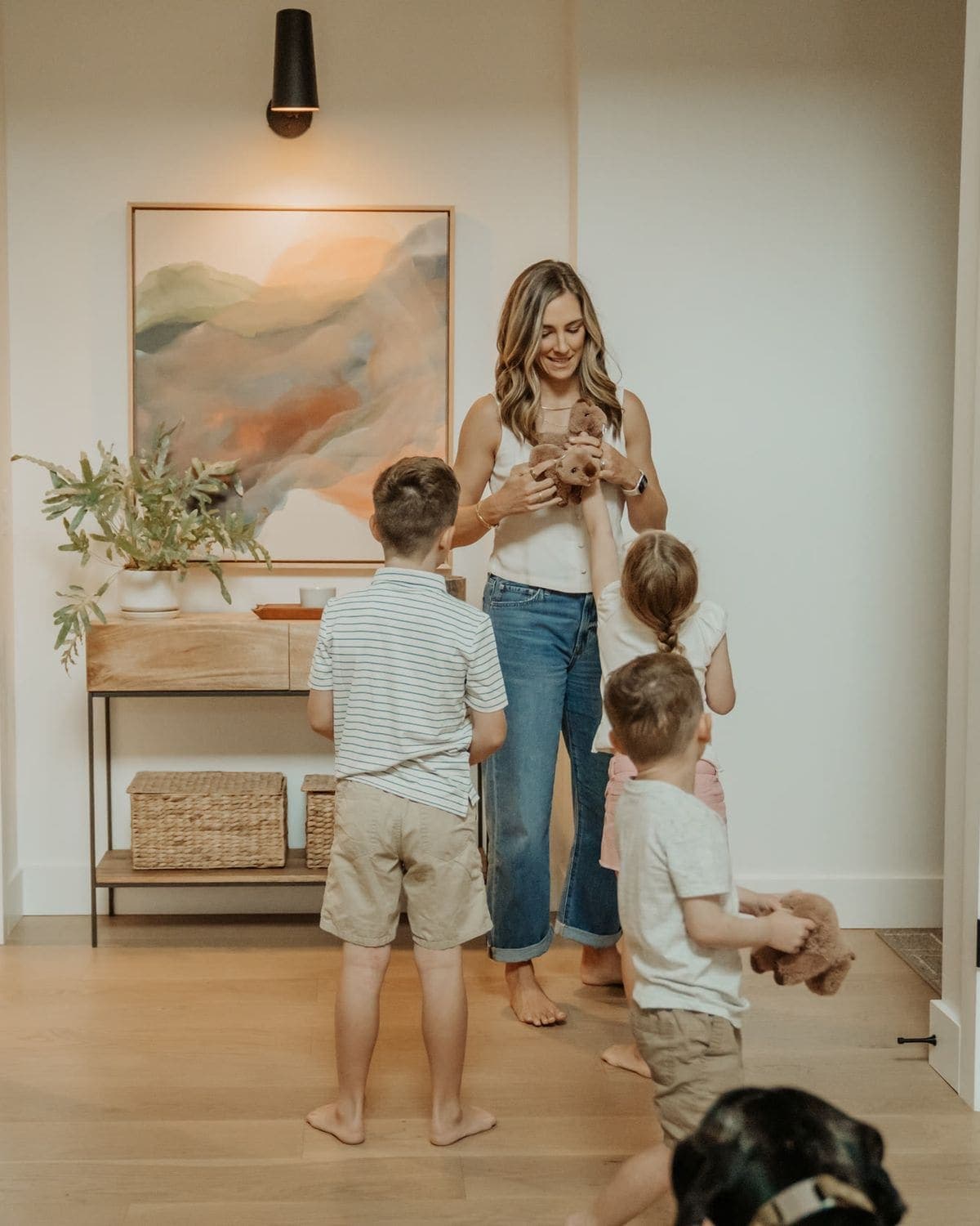 A parent greeting three children in the front hallway
