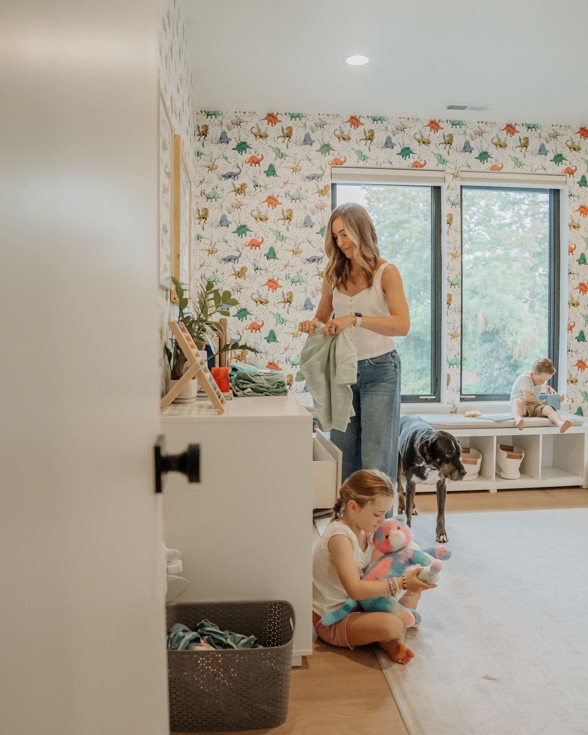 An adult folding children's clothes while a toddler plays on the bedroom floor