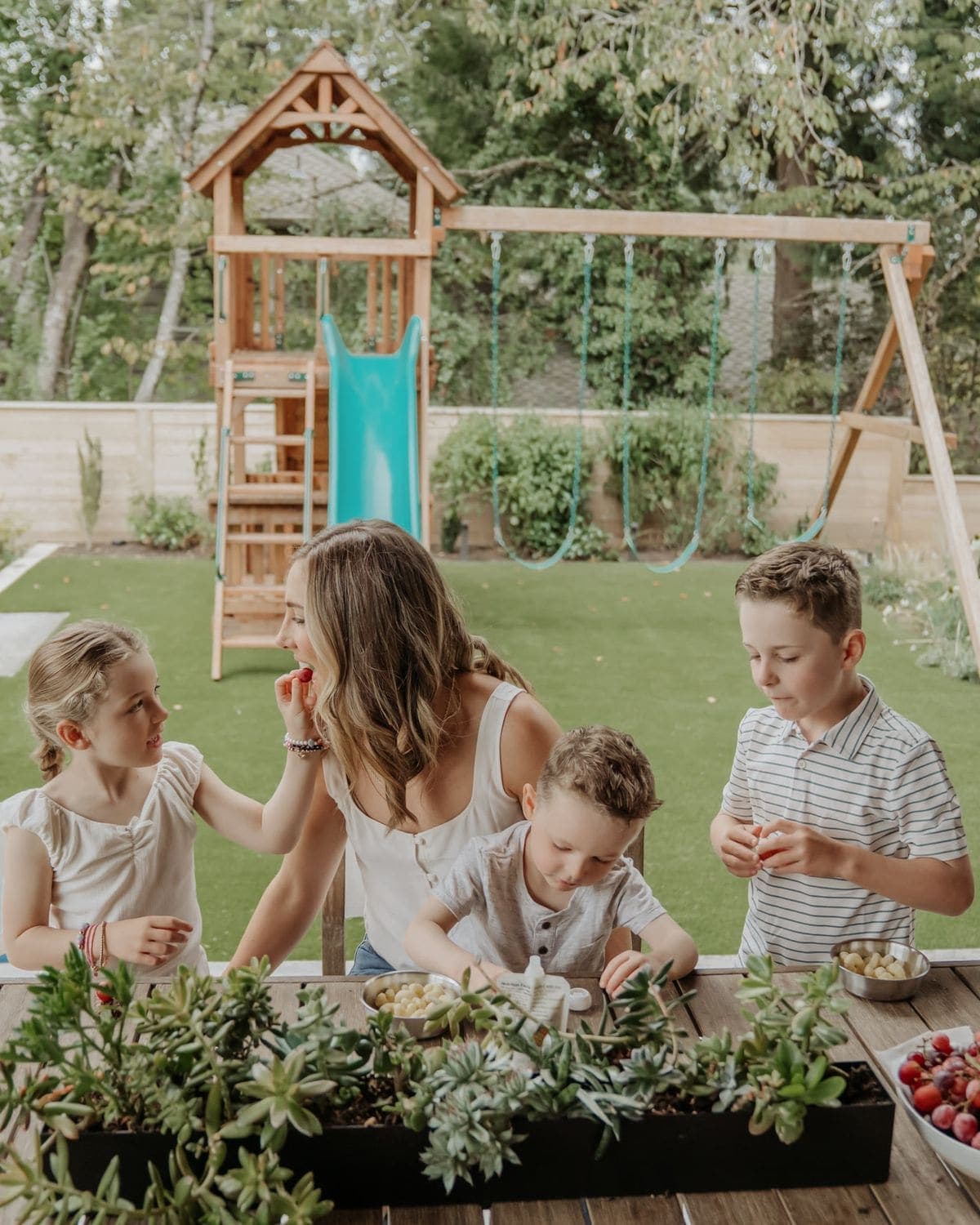 A parent and three children sharing a snack at a backyard table