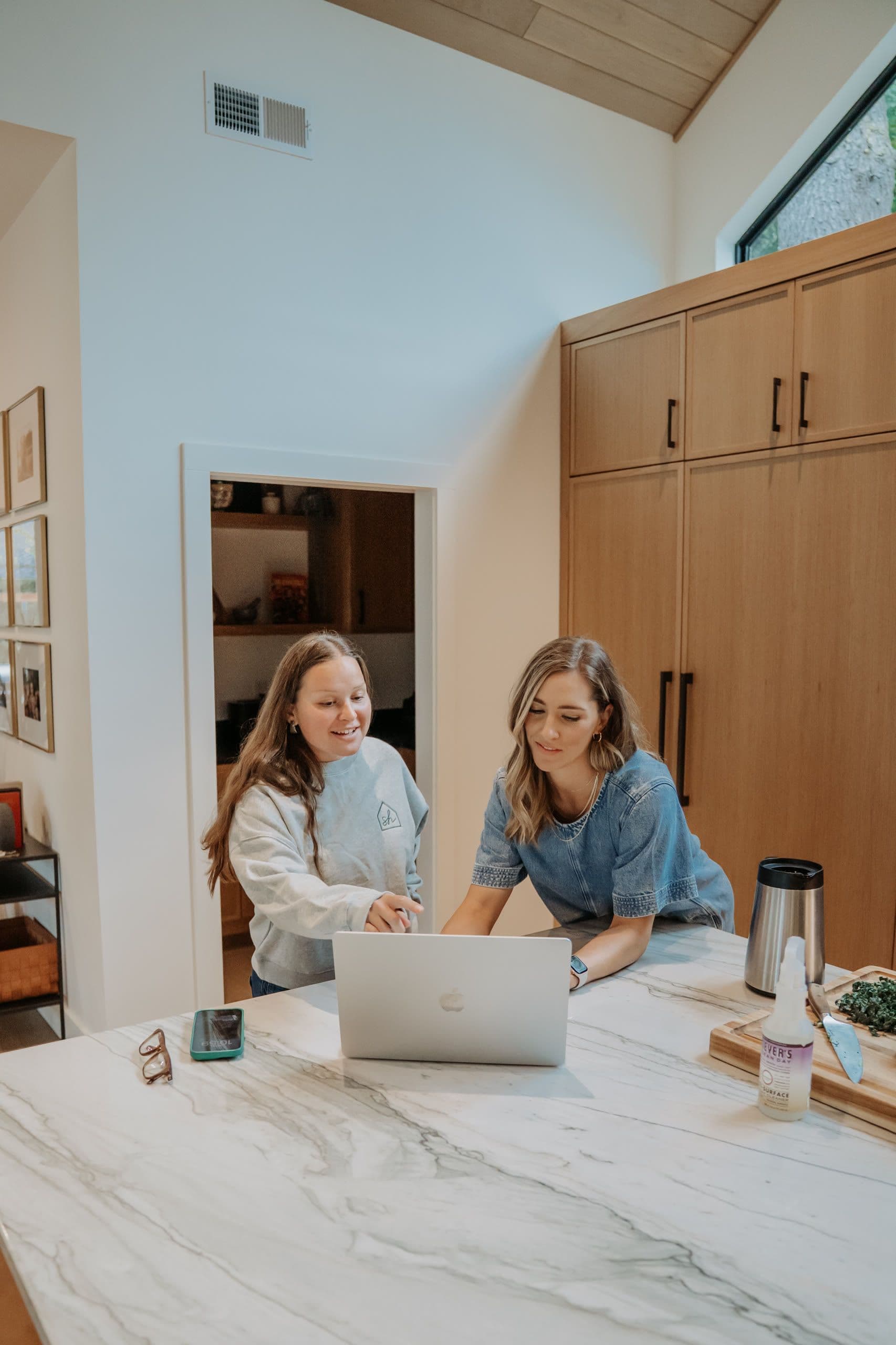 Two women working over a laptop at the kitchen table